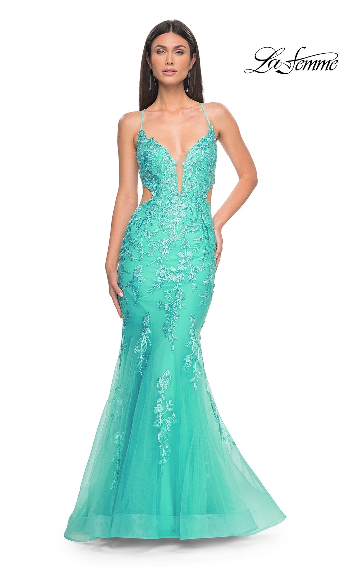 A woman wearing the La Femme Long Lace Mermaid Prom Dress 31133 in turquoise, featuring floral embroidery, sheer panels, and thin straps, stands against a white background.